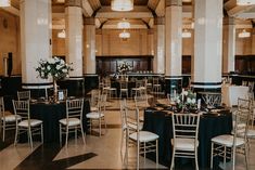 a room filled with tables and chairs covered in black tablecloths next to tall pillars