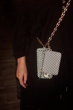 a woman wearing a black dress holding a white and black purse with a camera on it