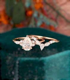 two diamond rings sitting on top of a green velvet covered box with flowers in the background