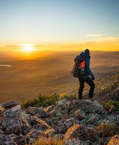 a man with a backpack is standing on top of a mountain looking at the sunset