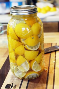 a jar filled with lemons sitting on top of a wooden table next to glasses