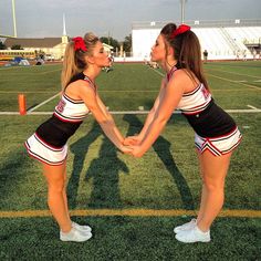 two cheerleaders holding hands on a football field