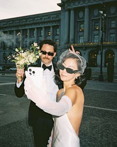 a man in a tuxedo holding a bouquet of flowers next to a woman wearing a veil