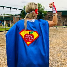 a woman in a blue cape and red glasses is standing on a playground with her arms up