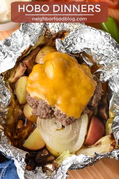 a hamburger covered in cheese and onions on top of aluminum foil next to some vegetables