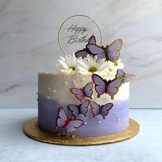 a birthday cake decorated with purple butterflies and white daisies on a gold platter