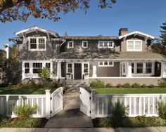 a large gray house with white trim on the front door and windows, surrounded by greenery