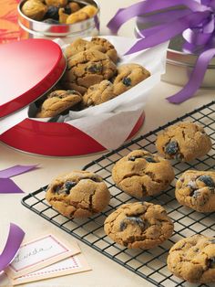 chocolate chip cookies are on a cooling rack next to a red box with purple ribbons