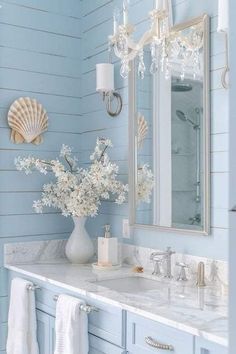 a bathroom with blue walls and marble counter tops, white flowers in a vase on the sink