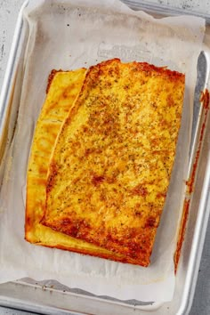 a square casserole dish with cheese and sauce on top, in a baking pan