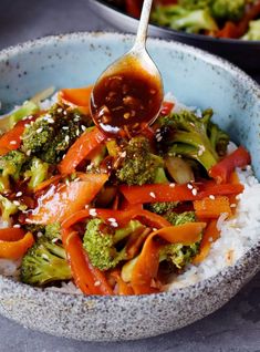 broccoli and carrot stir fry with rice in a blue bowl, with a spoon