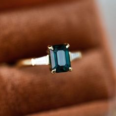 an emerald colored ring sits on top of a velvet box