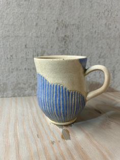 a blue and white cup sitting on top of a wooden table next to a wall