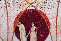 a man and woman standing next to each other in front of a flower covered wall