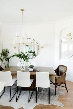 a dining room table with white chairs and a round mirror on the wall above it