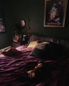 two cats laying on a bed in a dark room next to a lamp and pictures