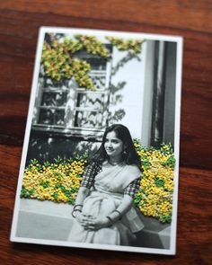 a black and white photo of a woman sitting in front of flowers on a wooden table