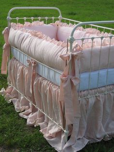 a baby crib with pink ruffles and bows on the bottom, sitting in grass