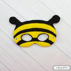 a yellow and black mask on a white wooden surface with the word bee written in it