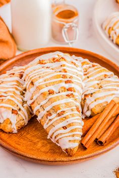 a plate topped with cookies covered in icing next to cinnamon sticks and a glass of milk