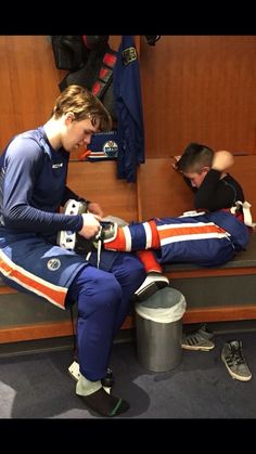 a young man sitting on top of a bench next to another person wearing an orange and blue uniform