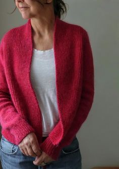 a woman wearing a red cardigan standing in front of a window with her hands on her hips