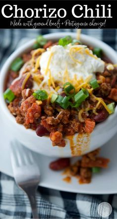 a white bowl filled with chili and sour cream on top of a blue checkered table cloth