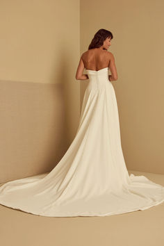 a woman in a white wedding dress is standing against a wall with her back to the camera