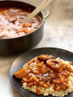 two black plates topped with food next to a pan filled with beans and meats