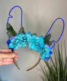 a hand holding a blue flower decorated headband