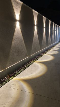 a long wall with lights on it next to a sidewalk