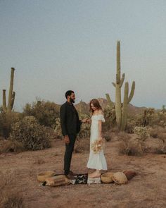 a man and woman standing next to each other in front of cacti on the ground