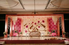 a stage set up for a wedding ceremony with pink and gold decorations on the wall