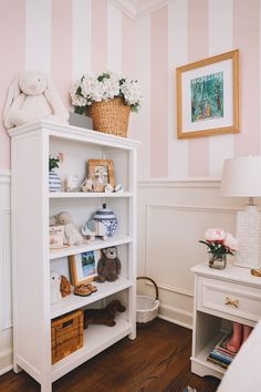 a white book shelf with stuffed animals and flowers on it in a room that has striped walls