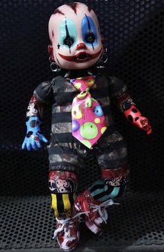 a creepy clown doll with colorful makeup and hair is sitting on a black surface in front of a mesh screen