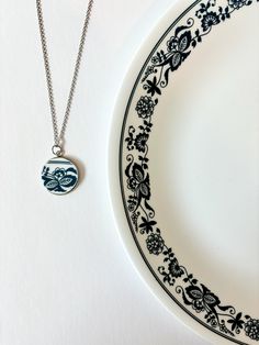 This blue floral nostalgic pendant necklace is handcrafted from an Old Town Blue Corelle plate, bringing memories of childhood to life in a beautiful, wearable form. Perfect for those who love vintage-inspired and sentimental jewelry, this piece combines personal history with eco-friendly craftsmanship. Pendant Width: 1/2 inch Pendant Height: 1/2 inch  The pendant suspends from a 18-inch stainless steel chain that secures with a lobster clasp.  Please note that due to the handmade nature of this piece, there may be slight variations and imperfections. These should be embraced as part of the unique charm and beauty of each piece! No two pieces are exactly alike, giving you a truly special and personalized accessory. Vintage Silver Necklaces With Birth Flower, Vintage Silver Necklace With Birth Flower, Vintage Silver Birth Flower Necklace, Vintage Everyday Necklace, Vintage Blue Flower Pendant Jewelry, Vintage Blue Flower Pendant Necklace, Vintage Everyday Charm Necklaces With Round Pendant, Vintage Blue Pendant Necklace, Vintage Birth Flower Pendant Jewelry