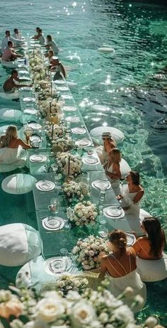 people sitting at tables in the water with flowers and plates laid out on them to look like they are floating