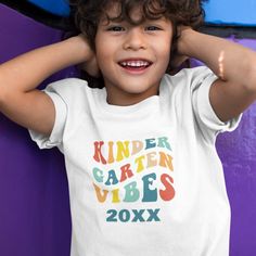 a young boy wearing a white shirt with the words kinder garden vibes on it