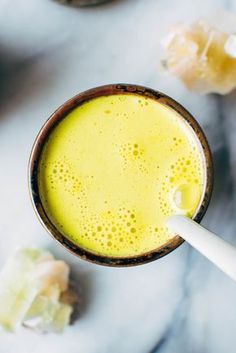 a glass filled with yellow liquid sitting on top of a white counter next to some pieces of fruit