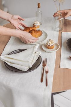 two people reaching for cupcakes on a table with white napkins and silverware