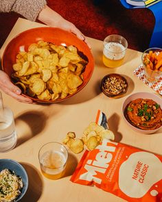 a table topped with bowls filled with food next to drinks and snacks on top of it