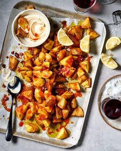 a tray filled with food next to two glasses of wine and some dipping sauces