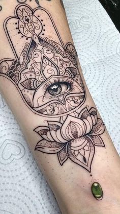 a hamsa tattoo on the arm with an eye and lotus flower in front of it