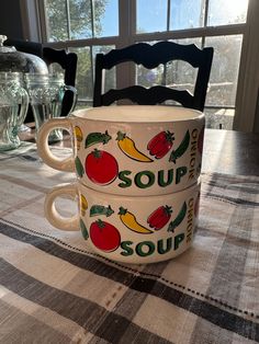 two soup mugs sitting on top of a checkered table cloth with the words soup in front of them