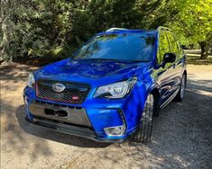 a blue subarunt parked in front of some trees