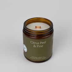 a candle that is sitting on top of a white surface with the words citrus peel and pine in front of it