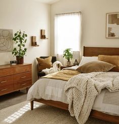 a bed room with a neatly made bed and two plants on the side of the bed