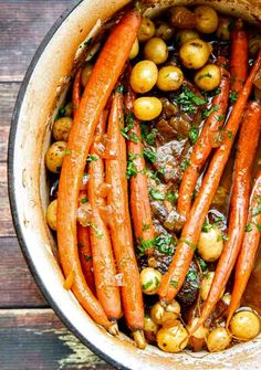 carrots, potatoes and other vegetables are in a pot on a wooden table top