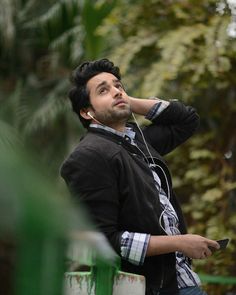 a young man listening to music with headphones on his ears while standing in the woods