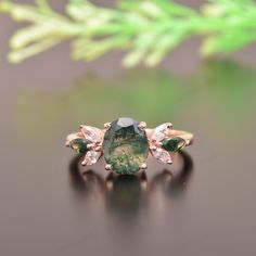 an emerald and diamond ring sitting on top of a black surface with green leaves in the background